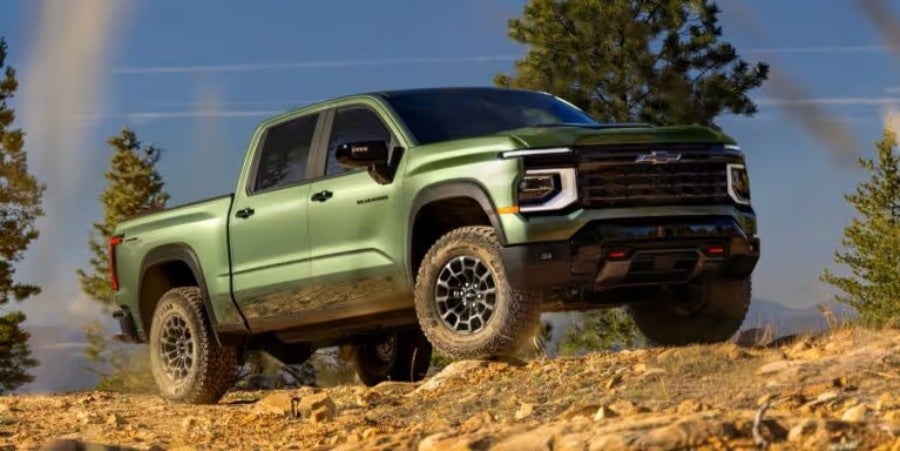 Green Chevrolet pickup truck drives up a rocky off-road incline under a blue sky.